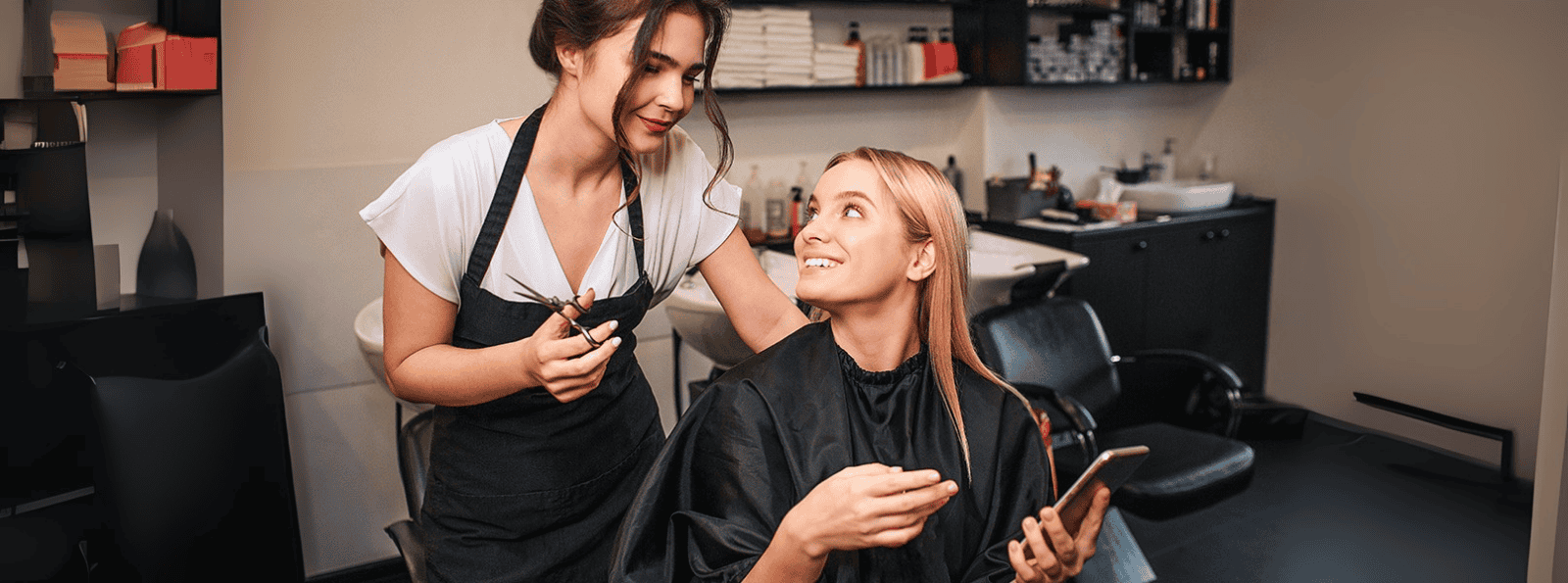 Hairdresser cutting a clients hair while she looks at her phone
