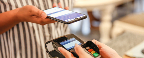 A person holds a smartphone in one hand and a credit card in the other, illustrating contactless payment methods.