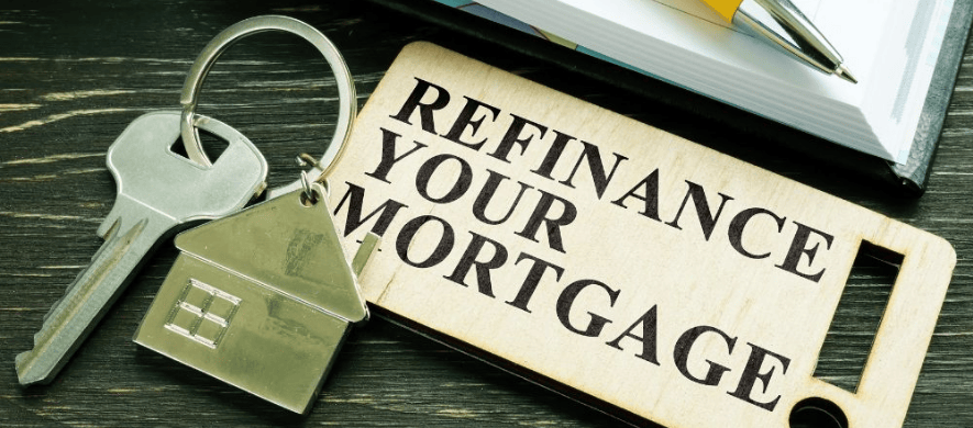 A close-up of a key with a keychain that reads “Refinance Your Mortgage” lays on a table next to a book that highlights the refinancing benefits banks offer.