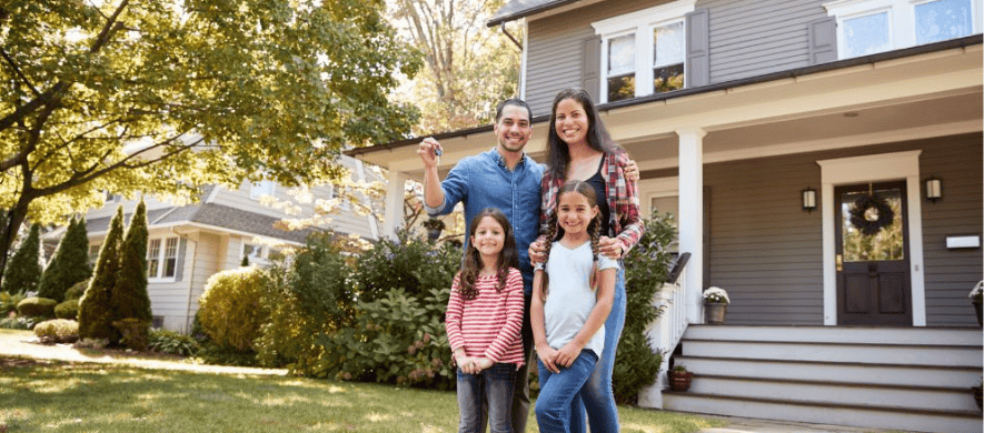 A family stands proudly in front of their house, showcasing their home, a result of personal loans for their dream purchase.
