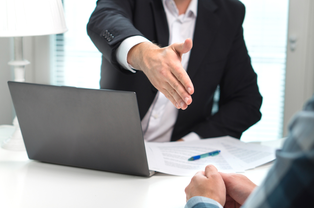 A male banker reaching his hand out to shake a customer's hand to congratulate them.
