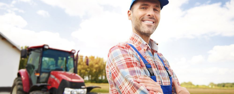 A farmer with his arms crossed stands next to a large red tractor after going through the agribusiness loans process.